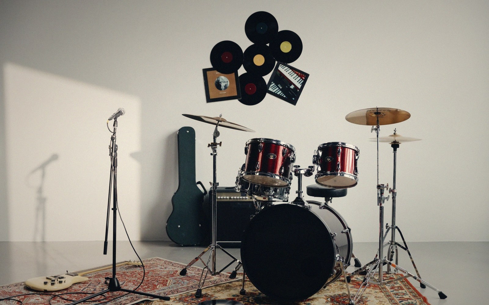 Drum kit, microphone stand and guitar case arranged in a studio with vinyl records on the wall
