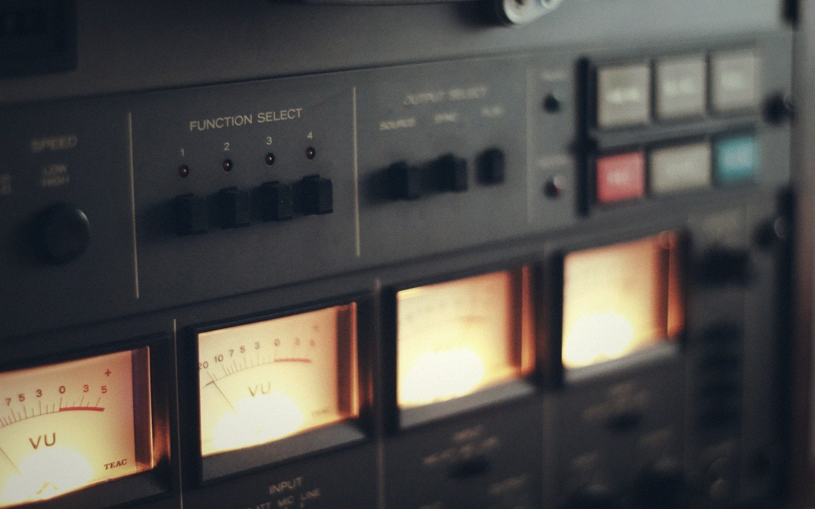 Close-up of a reel-to-reel tape recorder's illuminated VU meters and function select switches