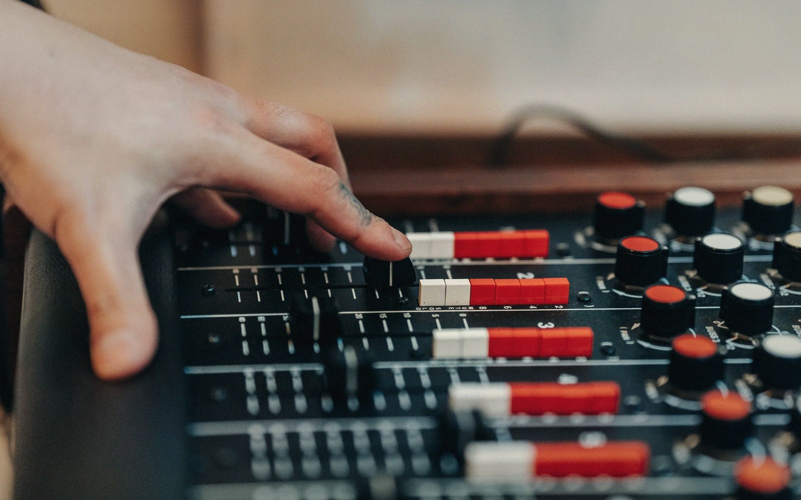 A finger adjusts a fader on an audio mixing console with rows of knobs
