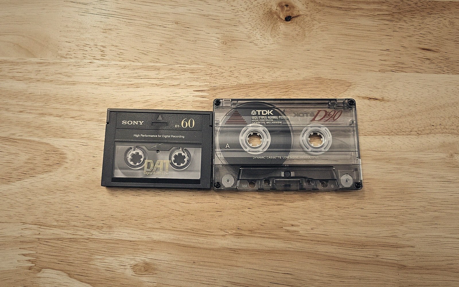 A Sony DAT tape and a TDK cassette tape lying side by side on wood